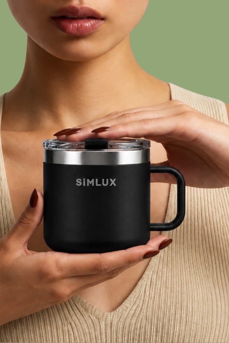Model cradling a Black SiMLUX Mug in both hands on a green backdrop