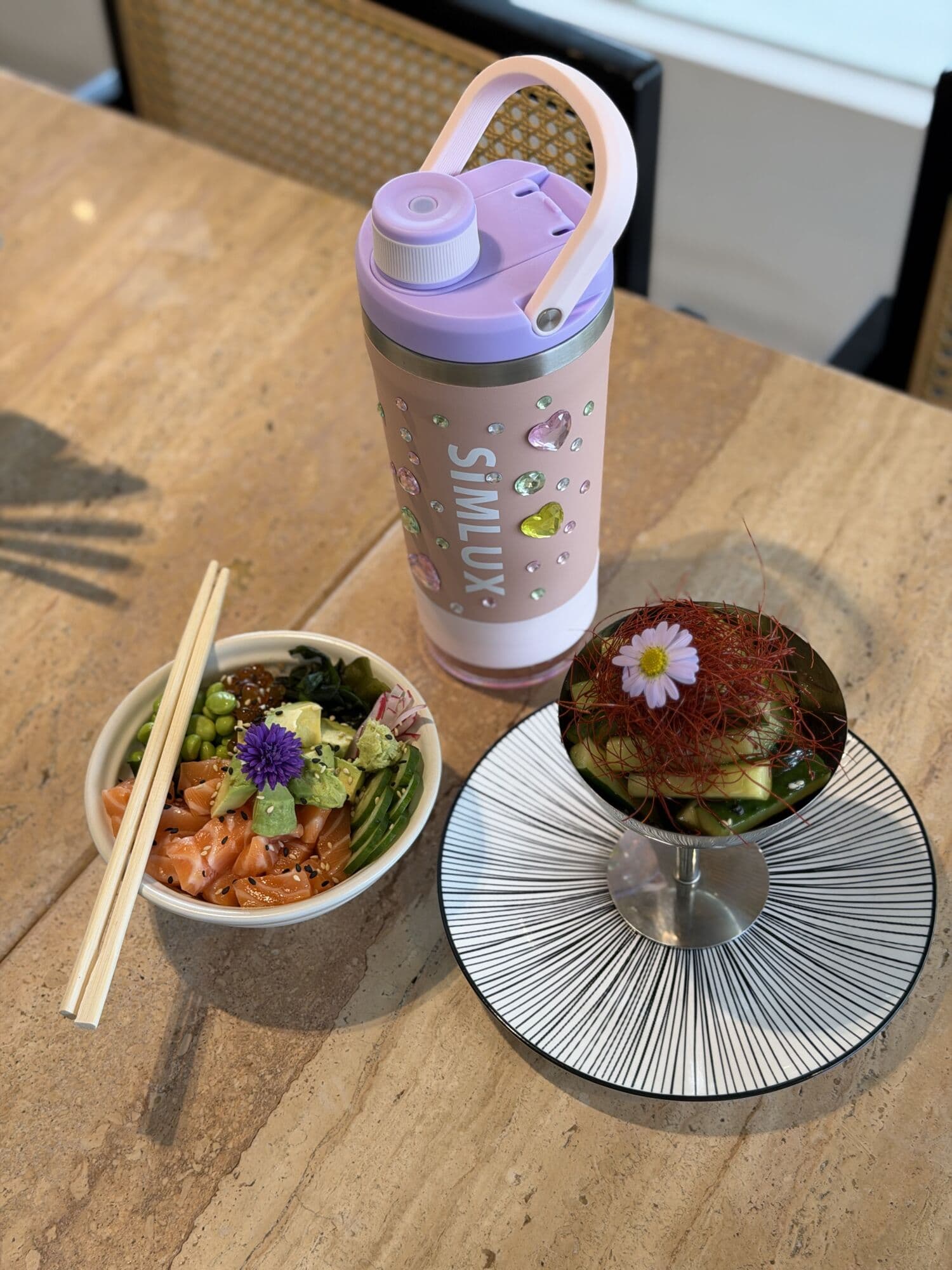 Pink shaker on a lunch table beside a poke bowl