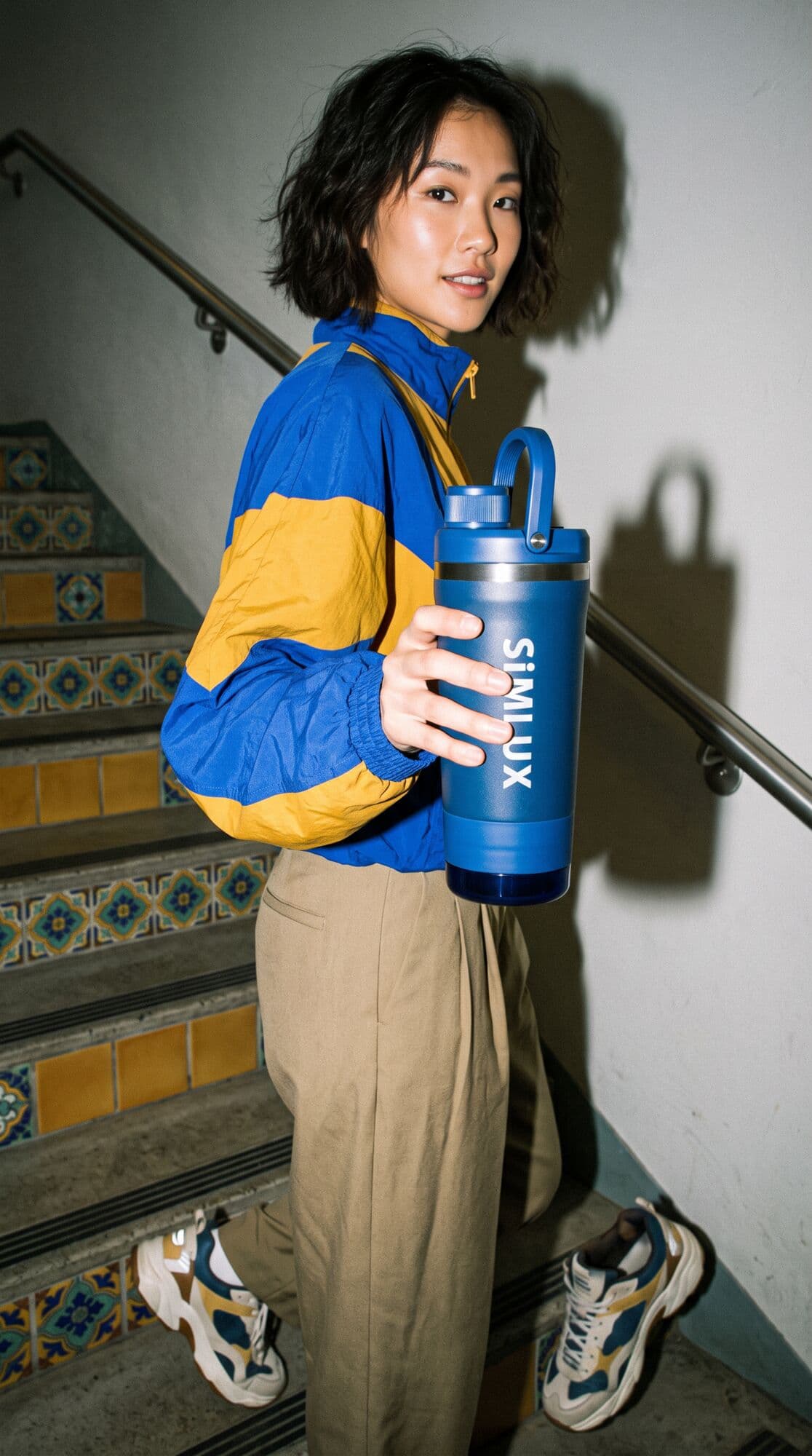 Model on a tiled stairway holding out a Blue shaker
