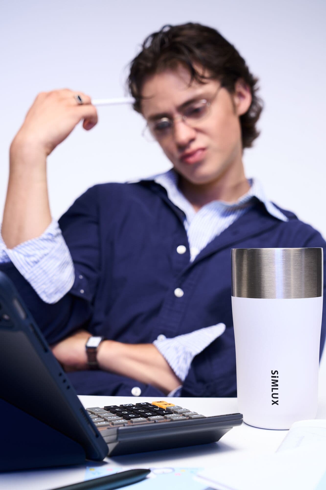 Model at a desk with a white coffee tumbler and calculator