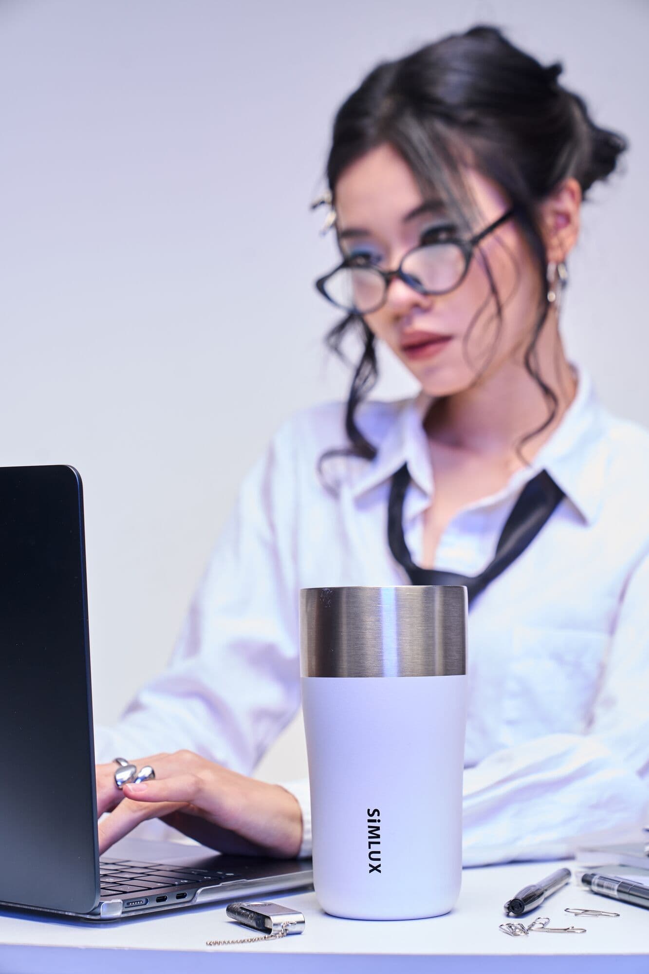 Two models at a laptop with a grey coffee tumbler