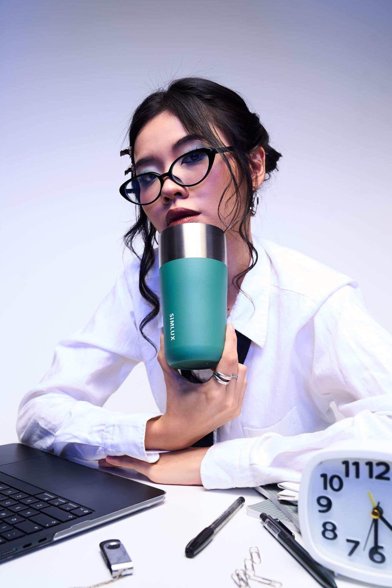 Model sipping from a green coffee tumbler at her desk