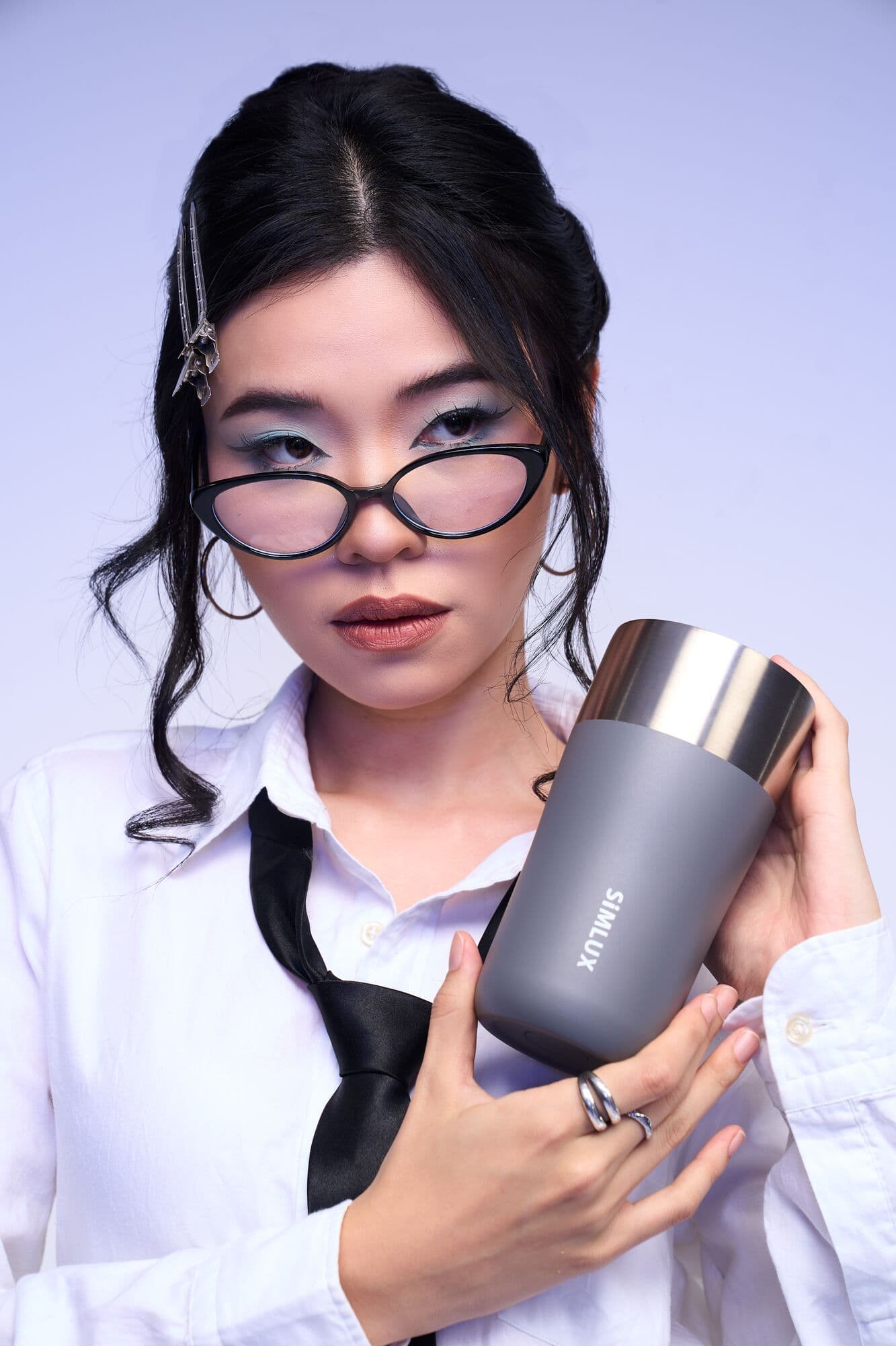 Model in cat-eye glasses holding a grey coffee tumbler